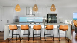 A modern kitchen with a central island, bar stools, pendant lights, and a large window overlooking the ocean. - Luxurious Terrace Hideaway with Heated Pool (Ocean Grove)