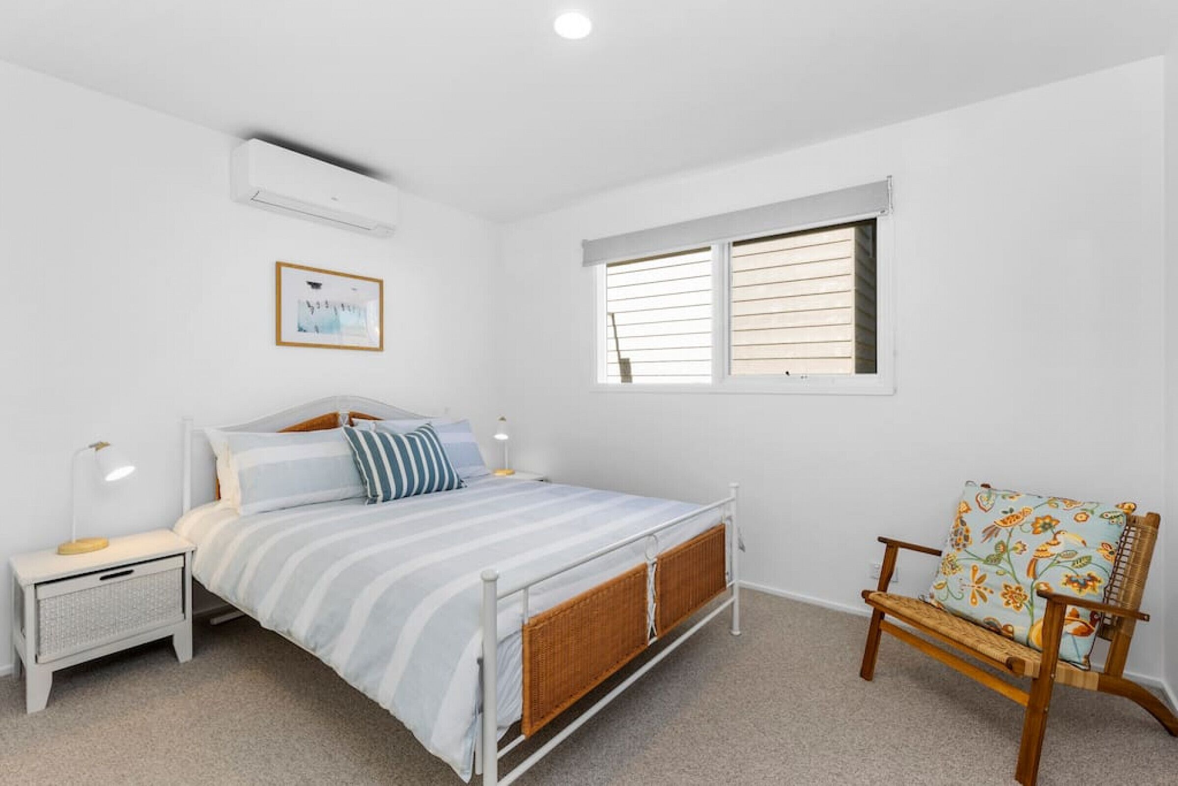A bedroom with a bed, bedside tables, a chair, a window, and an air conditioning unit.