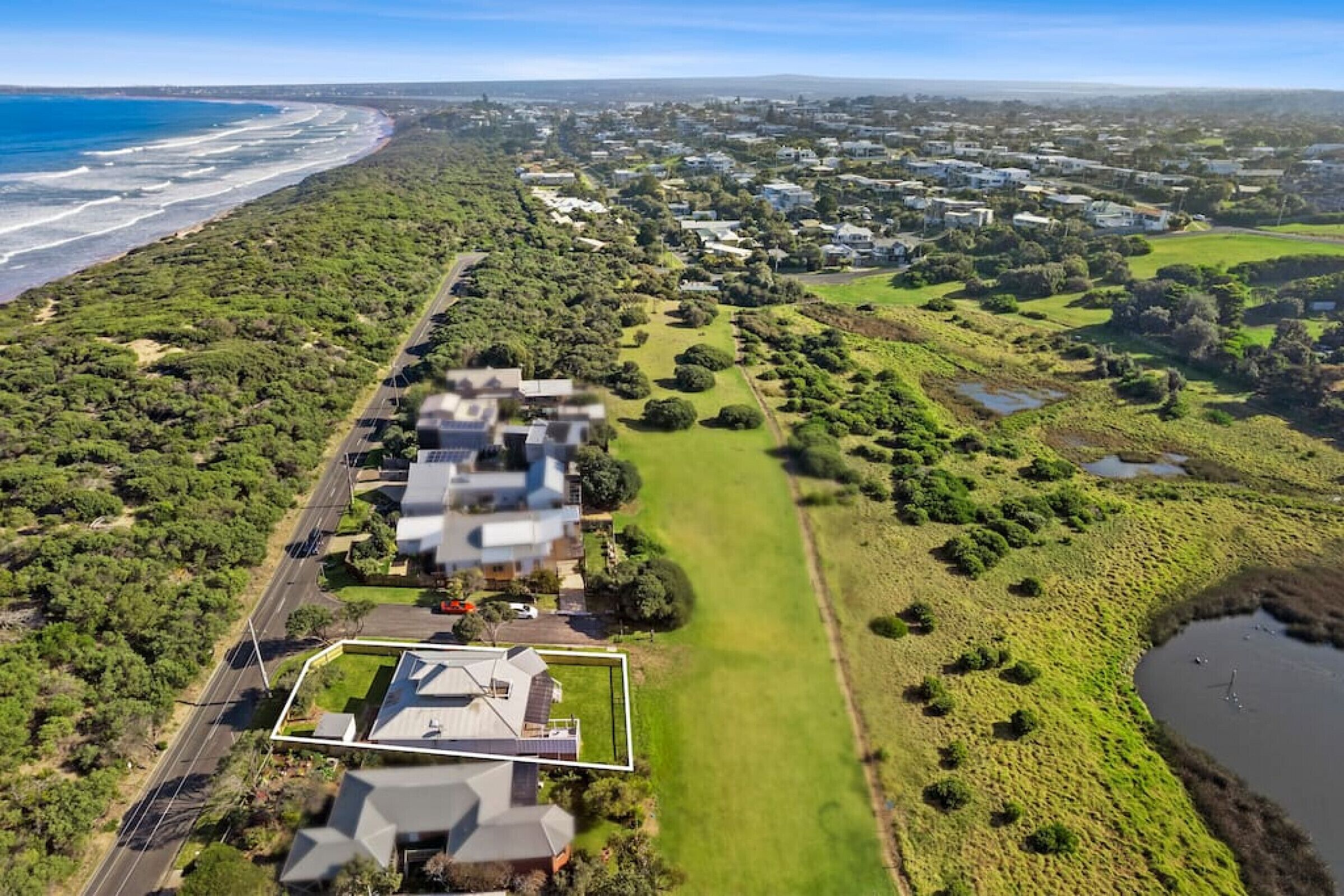 An aerial view of a coastal residential area with houses, a golf course, and a beach.