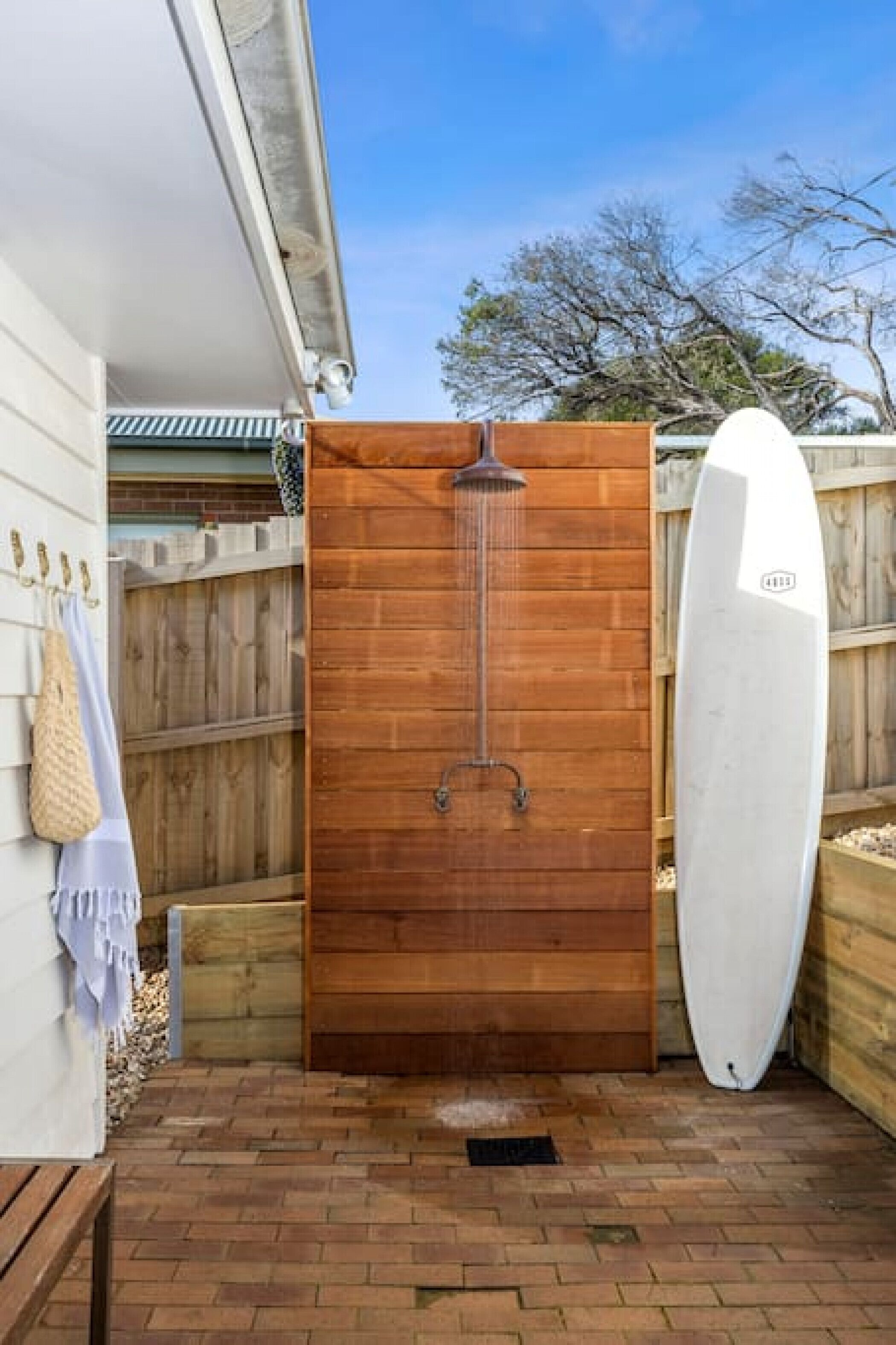 A wooden door with a showerhead, a white surfboard, and a brick patio.