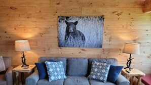 A cozy living room with a grey sofa, patterned cushions, two wooden side tables with lamps, and a bear-themed wall art.