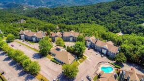 An aerial view of a residential area with multiple houses, a swimming pool, and a mountainous backdrop.