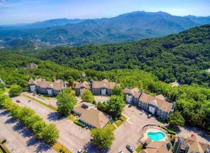 An aerial view of a residential area with multiple houses, a swimming pool, and a mountainous backdrop.