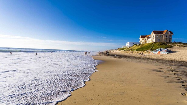 A beach with a large building on a hill, sandy shore, and ocean waves.