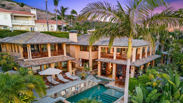 Un'ampia casa a più piani con piscina, area salotto esterna e rigogliosa vegetazione tropicale.