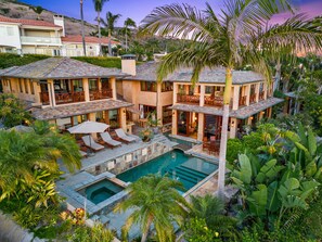 A large, multi-story house with a swimming pool, outdoor seating, and lush tropical landscaping.