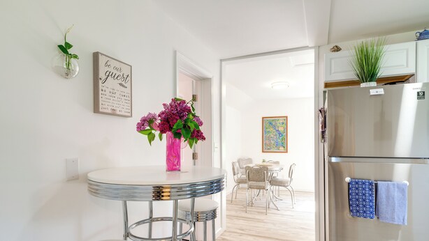 A modern kitchen with a stainless steel refrigerator, a round dining table with bar stools, and a decorative vase with flowers. - 3 Mi to Lake Michigan: ‘The Country Cottage’ (Central Lake)
