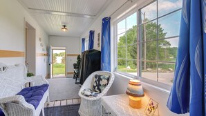 A room with a wicker sofa, a chair, a table with a candle, and a view of the outdoors through large windows. - 3 Mi to Lake Michigan: ‘The Country Cottage’ (Central Lake)