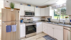 A modern kitchen with white cabinetry, stainless steel appliances, a built-in oven, and a window with a view of greenery. - 3 Mi to Lake Michigan: ‘The Country Cottage’ (Central Lake)