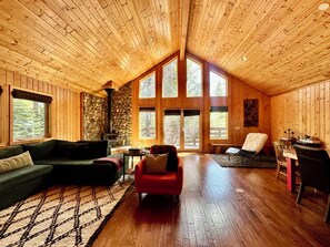 A log cabin interior with a stone fireplace, wooden walls, and large windows.