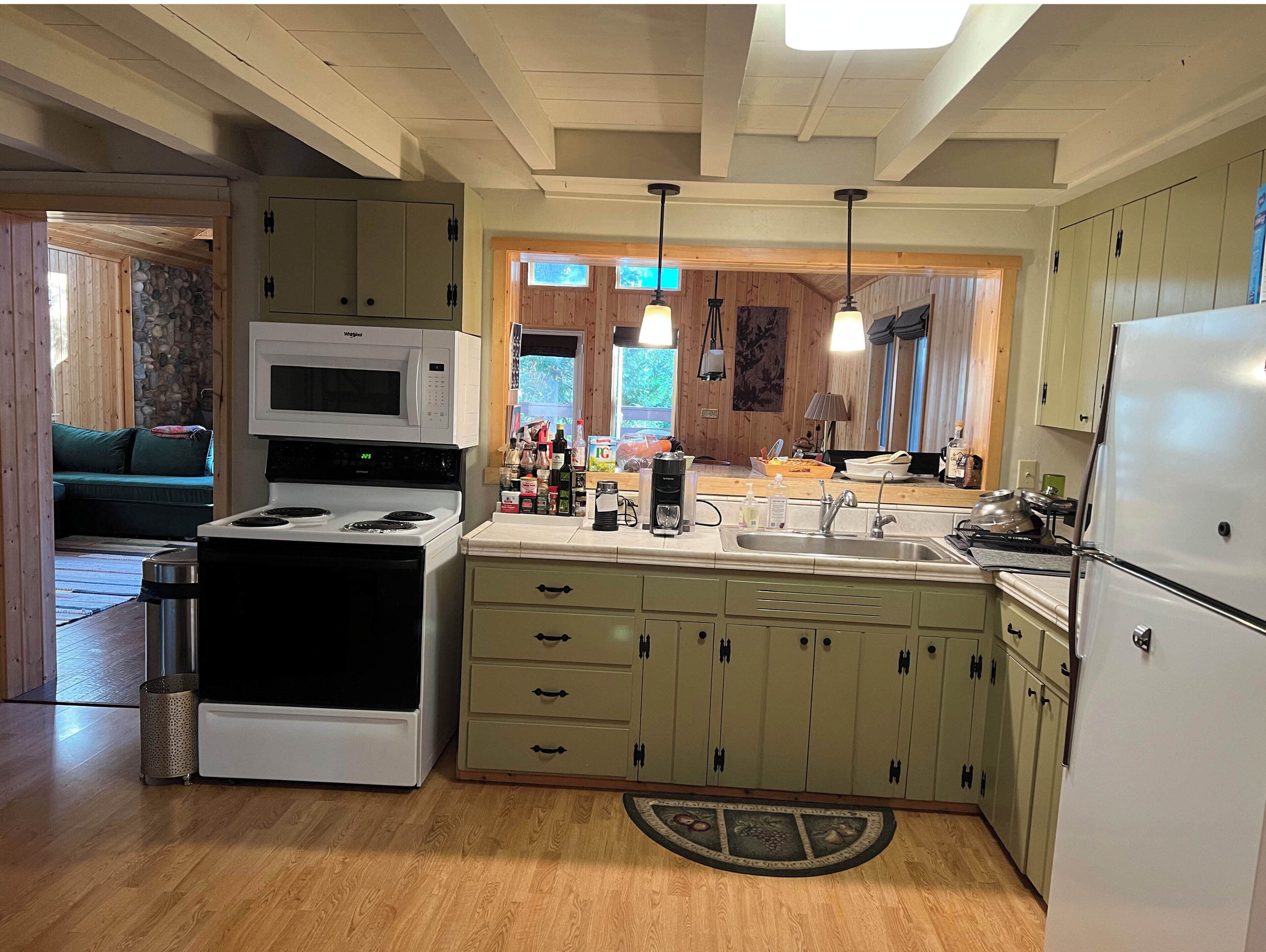 A kitchen with wooden cabinets, a stove, a microwave, a sink, and a refrigerator.