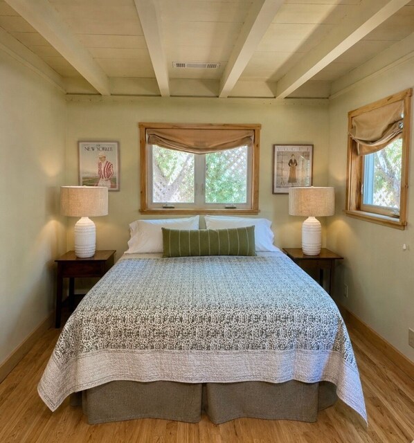A bedroom with a large bed, two bedside tables with lamps, a window with a view, and two framed pictures on the wall.