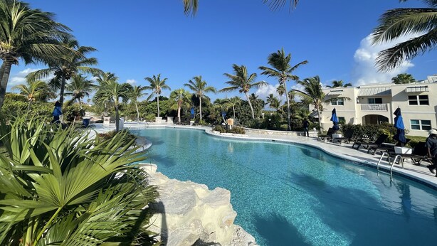 Un área de piscina con agua azul cristalina, rodeada de palmeras y un edificio con balcón.