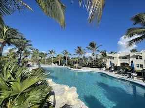 A pool area with clear blue water, surrounded by palm trees and a building with a balcony.