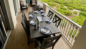 Un balcón con una mesa de comedor para cuatro personas, con vistas a un paisaje exuberante y el mar.
