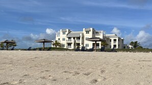 Une vaste propriété en bord de mer, comprenant plusieurs étages, dotée d’un patio couvert et de plusieurs chaises longues.