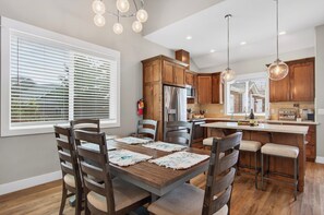 Une cuisine moderne avec des meubles en bois, un îlot central, des tabourets de bar et une table à manger avec des sets de table.