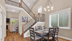 Un coin repas avec une table et des chaises en bois, un escalier avec des rampes en bois et un lustre.