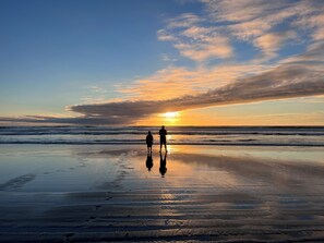 A beach scene with two people walking on the shore, waves, and a sunset.