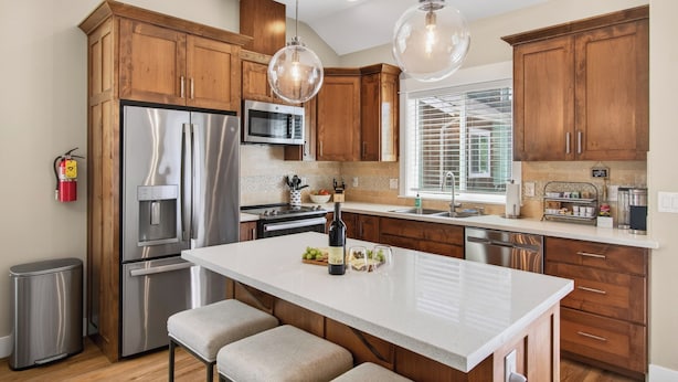 Une cuisine moderne avec des meubles en bois, des appareils en acier inoxydable, un grand îlot central et des luminaires suspendus.