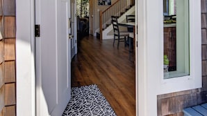 Une façade en bois avec une porte blanche, un escalier et un coin repas comprenant des chaises et une table.