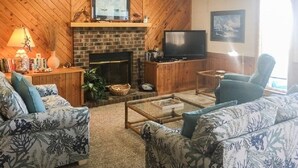 A living room with a brick fireplace, a flat-screen TV, and two patterned sofas. - Oceanfront townhome with sound access in Duck! (Duck)