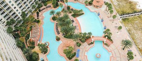 A large hotel with multiple swimming pools, palm trees, and a central fountain.