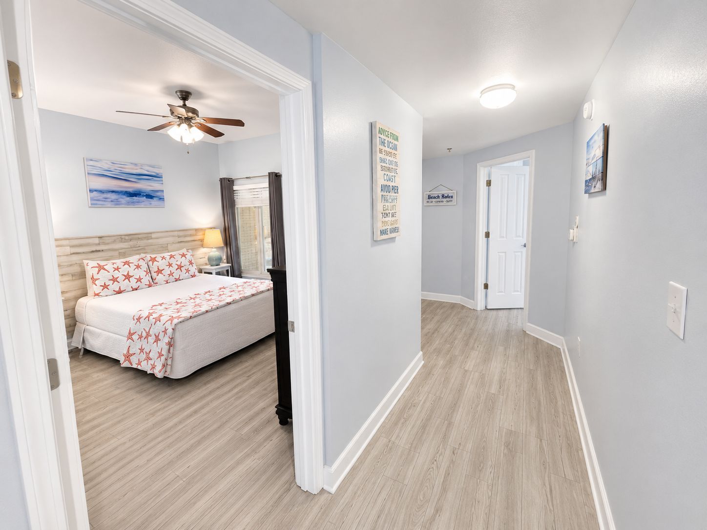 A hotel room with a bed, a ceiling fan, a nightstand, a lamp, and a window with curtains.