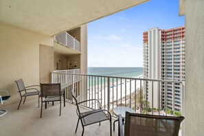 A balcony with chairs and a table, overlooking a beach and a tall building.