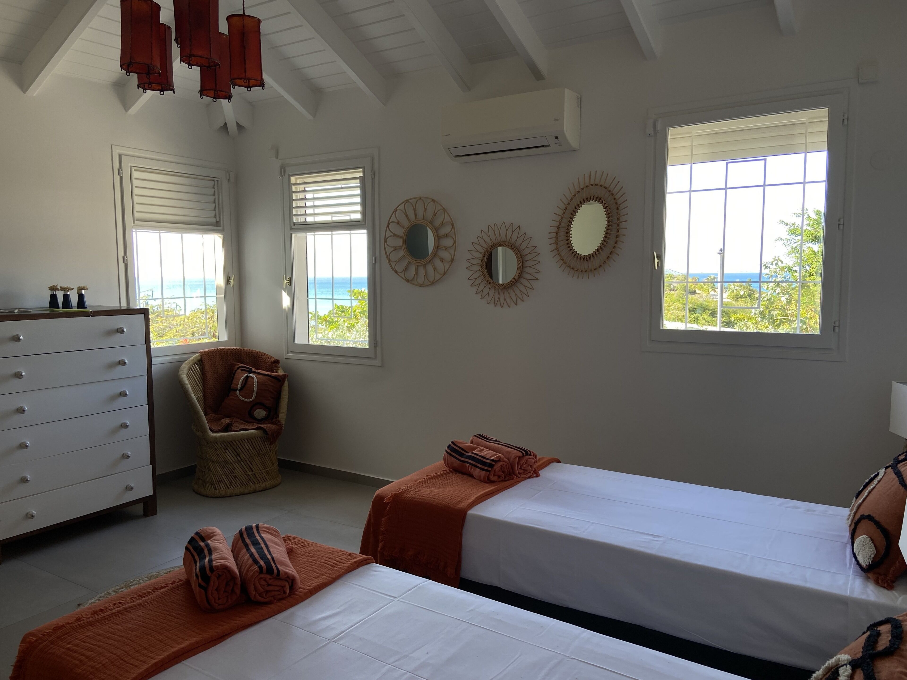 Quarto com duas camas, cômoda e duas janelas com vista para o oceano.