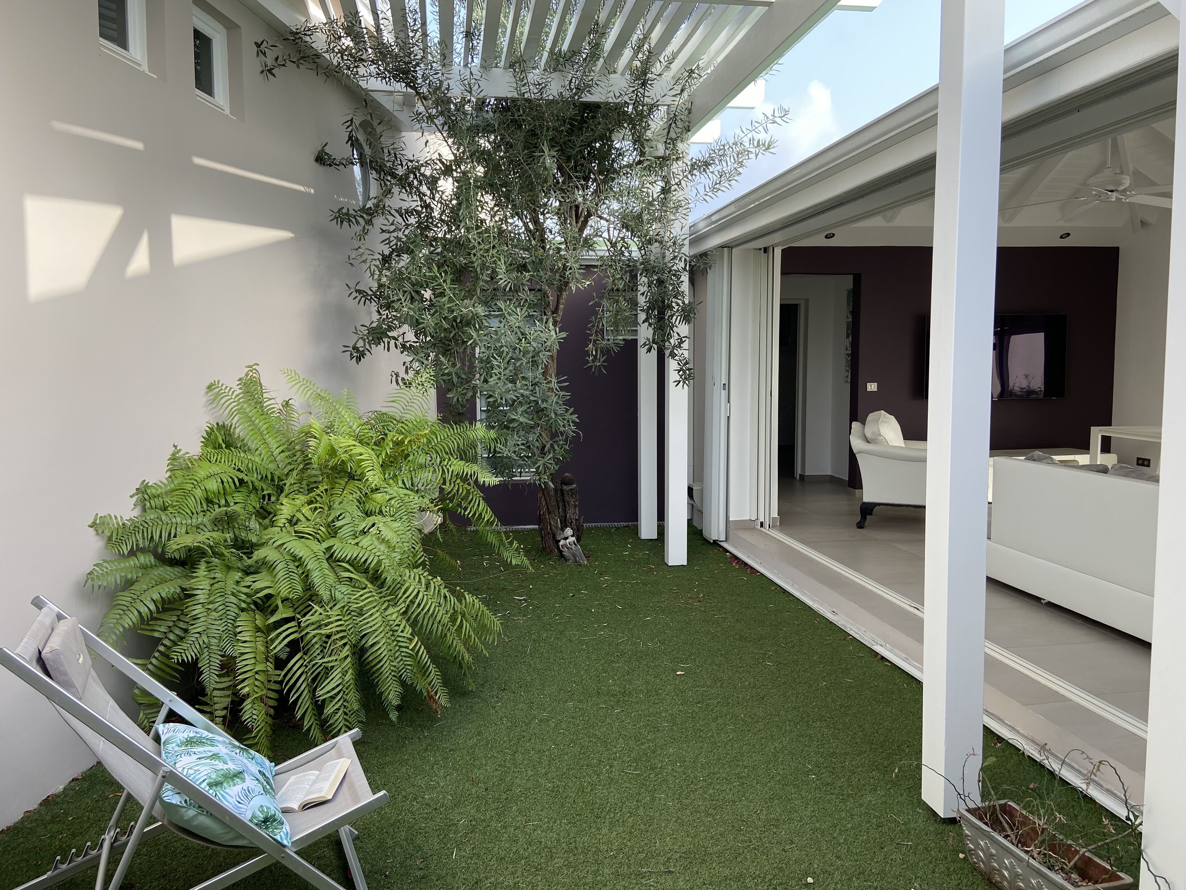 A modern outdoor area with artificial grass, a white chair with a cushion, and a large fern plant.