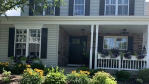 A two-story house with a front porch, stone foundation, and a well-maintained garden with various plants and flowers. - Idyllic Country Living (Geneva)