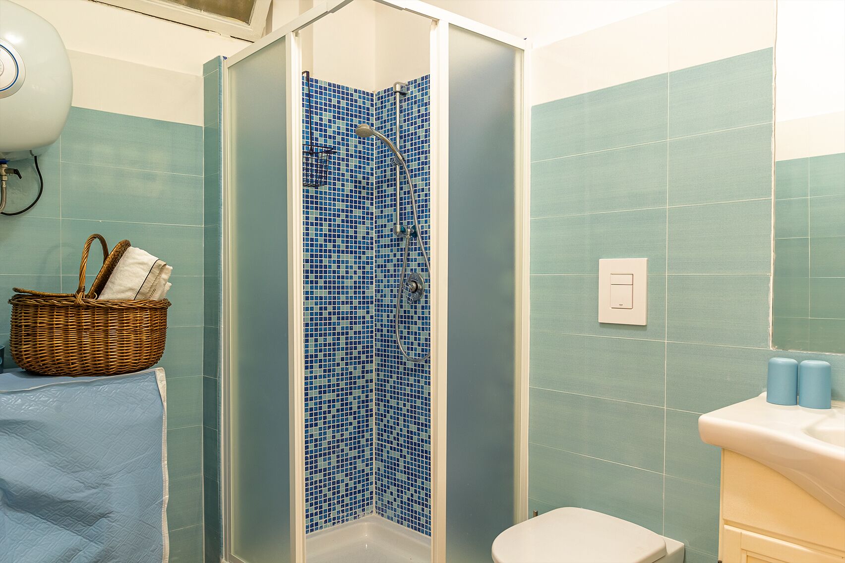 A bathroom with a shower, a toilet, a sink, and a basket of toiletries.