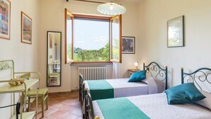 Un dormitorio con dos camas, un escritorio, una silla, una ventana con vistas y un radiador.