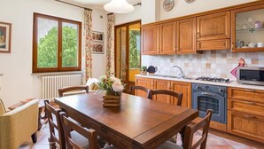 Una cocina con armarios de madera, una mesa de comedor y un ventanal con cortinas.