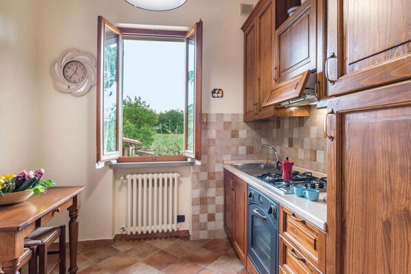 Una cocina con armarios de madera, una estufa y un ventanal con una persiana abierta.