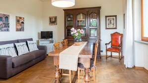 A living room with a sofa, dining table, chairs, a television, and a cabinet with glass doors. - Santa Margherita - NINFEA (Poggibonsi)