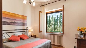 Un dormitori amb un llit, una finestra amb vista a arbres, un radiador i un quadre al mur.