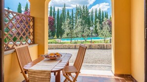 Terrassa exterior amb taula i caires de fusta, vista a una piscina i arbres, i una paret groga.