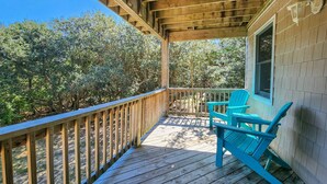 Une terrasse en bois avec une rambarde, deux fauteuils Adirondack turquoise et une fenêtre avec un luminaire.