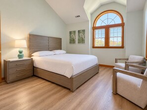 A bedroom with a bed, a nightstand, a chair, and a window with blinds.