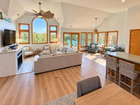 Una sala de estar amplia con un sofá grande, una zona de comedor con mesa y sillas, y una cocina con televisor y armarios.