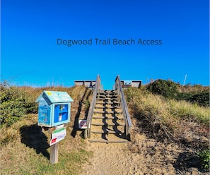 Una escalera de madera que da acceso a la playa, con un buzón y un cartel a la izquierda.