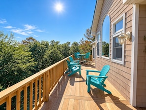 Una terraza de madera con mobiliario exterior y vista a una casa.