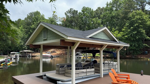 Ein überdachter Steg mit Sitzgelegenheiten und einem kleinen Pavillon, ein anlegender Bootsanleger und ein ruhiger See mit Bäumen im Hintergrund.