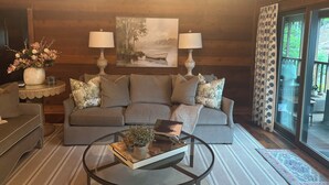 Ein gemütliches Wohnzimmer mit einer Couch, zwei Lampen, einem Gemälde und einem Glastisch.