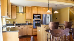 Une cuisine dotée de meubles en bois, d’appareils électroménagers en acier inoxydable et d’un îlot central avec des chaises.