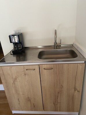 Compact kitchen with stainless steel sink, coffee maker, and wooden cabinets.