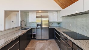 Een moderne keuken met een roestvrijstalen koelkast, een ingebouwd waterdispenser en een zwart inductiekookplaat.