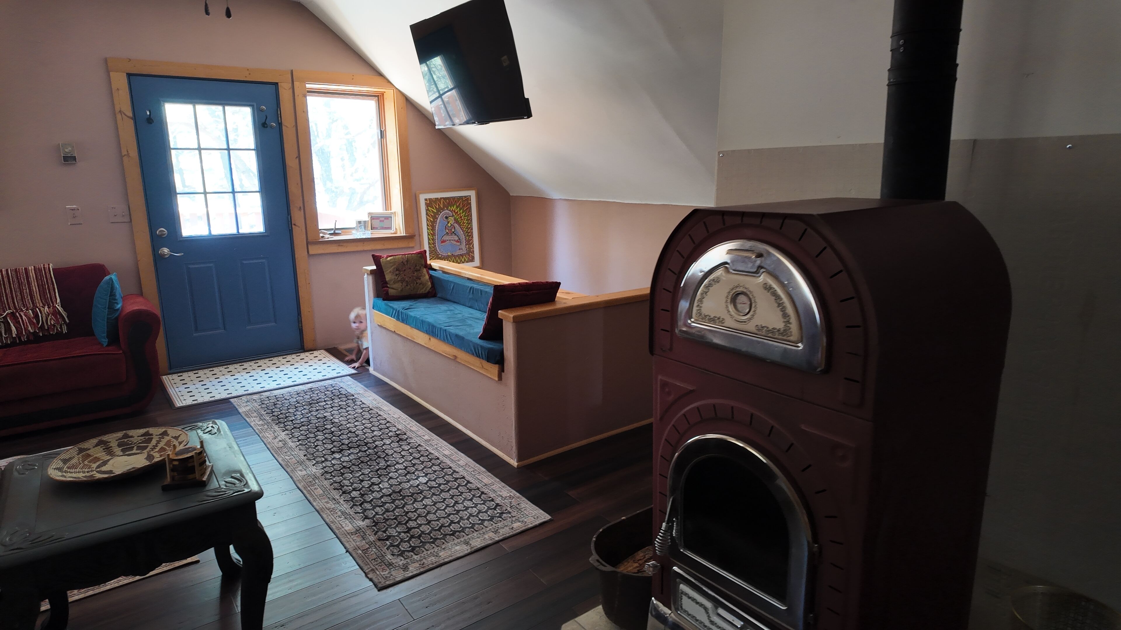 Un salon chaleureux avec une porte bleue, un canapé rouge, un banc bleu, un tapis à motifs et une cheminée.